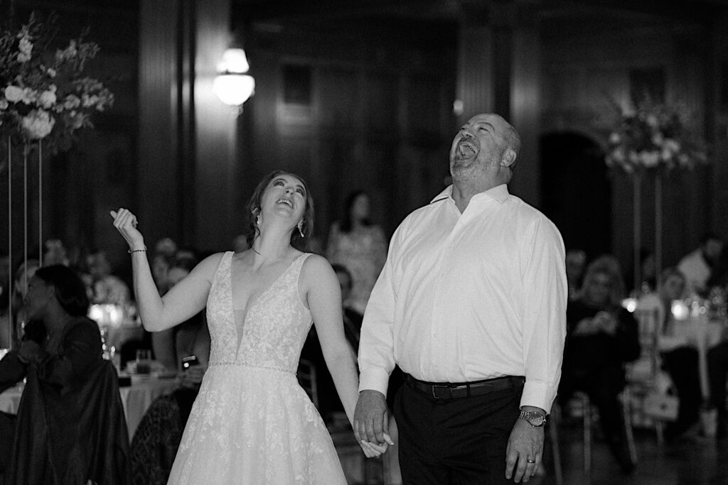 Bride holds hands with her father and look up at the ceiling during wedding reception in Indianapolis. 