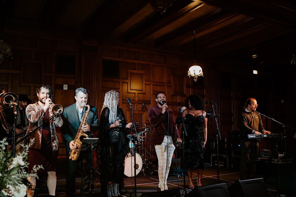 Live band with trumpet, saxaphone, keyboardist and singers play in gorgeous 1920's reception room during LGBTQ+ wedding reception. 