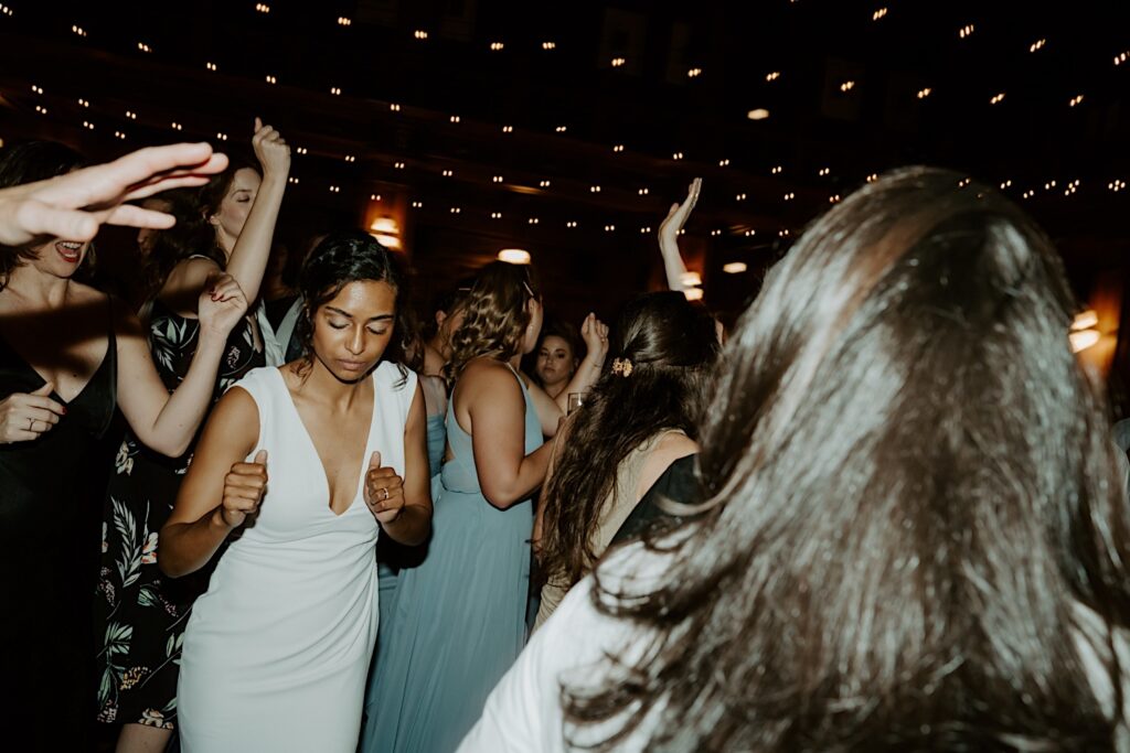 Bride dances among guests during wedding reception with string lights above them. 