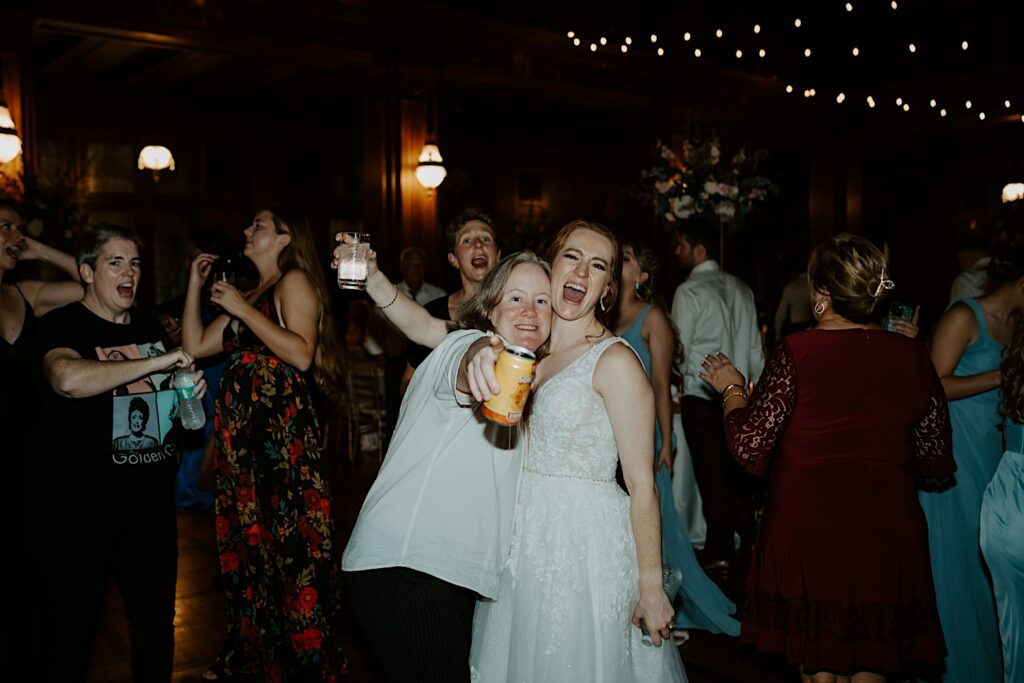 Bride smiles at the camera with a guest as the guest points to the camera holding a beer during wedding reception in Indianapolis. 