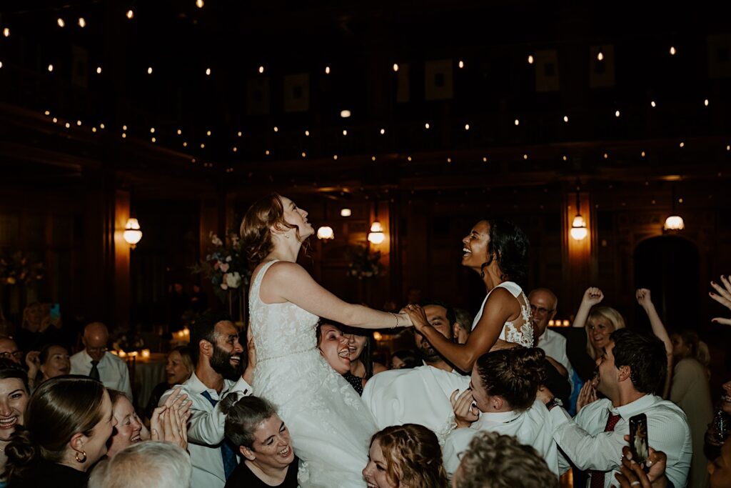 Guests hold up bride's on their shoulders during wedding reception as they sing.