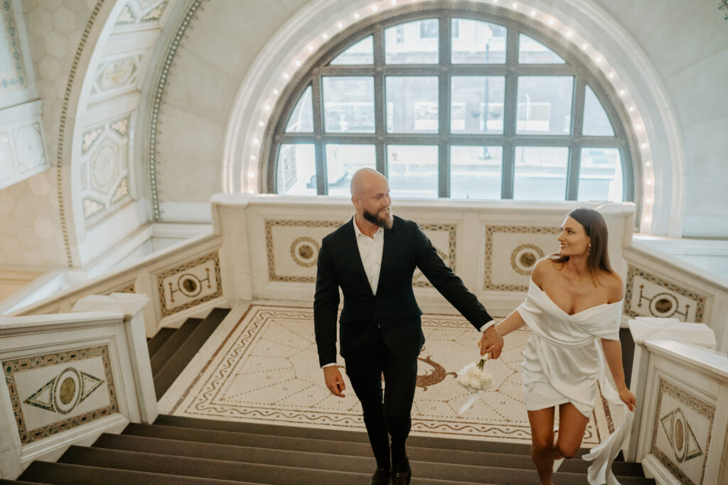 Couple walks up the steps of the Chicago Cultural Center for Engagement portraits smiling at each other. 