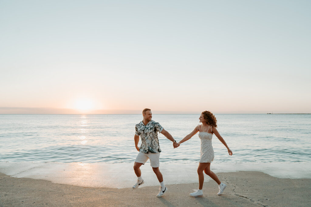 A Couple runs across a beach with the lake behind them at sunset for gorgeous casual engagement photos in Chicago. 