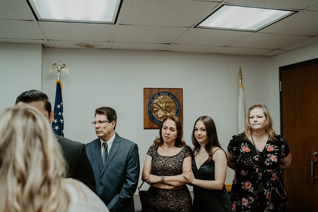 Bride and Groom's families stand and watch elopement ceremony in City Hall room. 