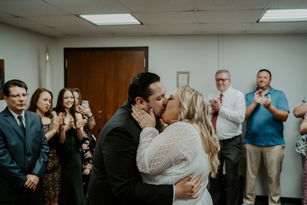 Bride and Groom kiss during intimate elopement ceremony while their families clap behind them. 