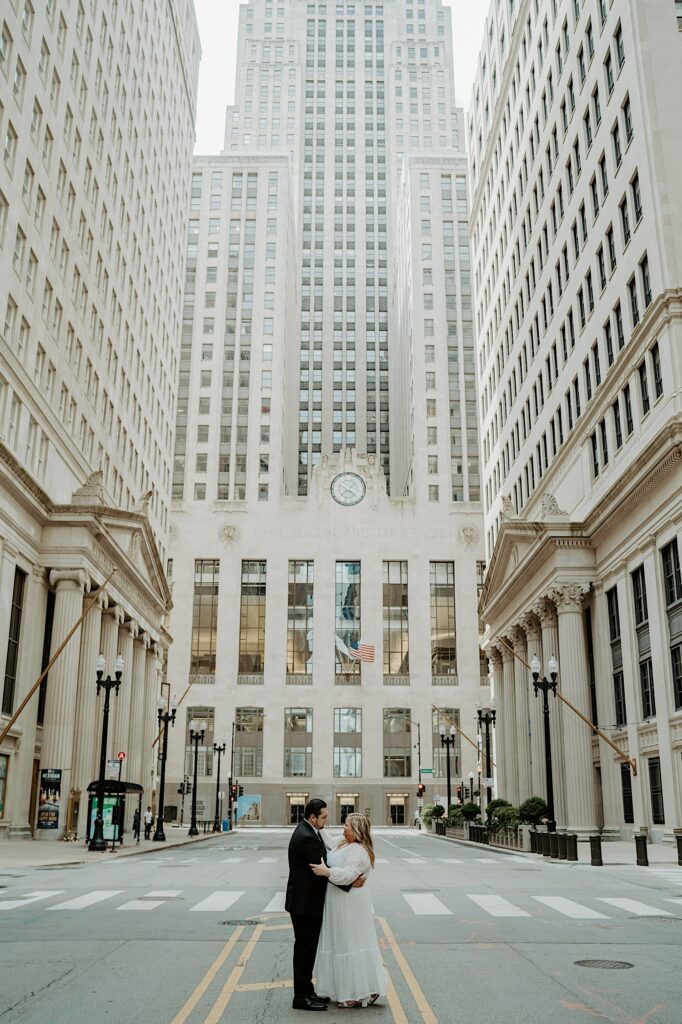 Bride and Groom stand in the center of a street in front of Chicago Board of Trade Building and look at each other. 