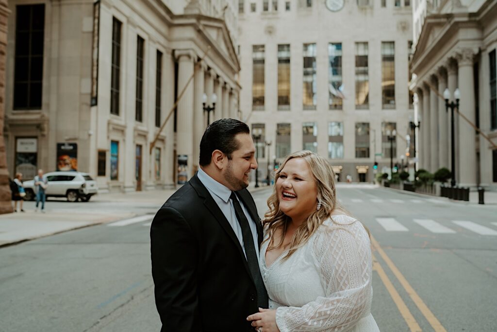 Bride and Groom pose candidly for Elopement portraits in the center of a Chicago street with columned buildings around them. 