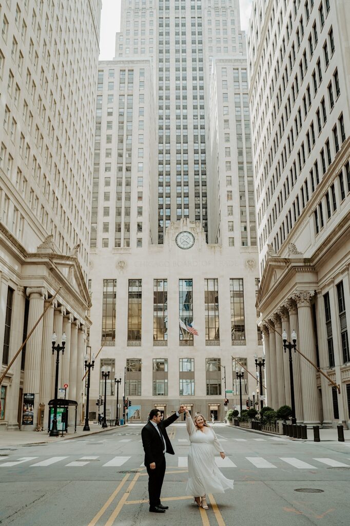 Bride and Groom dance in the center of a street in front of Chicago Board of Trade Building and look at each other. 