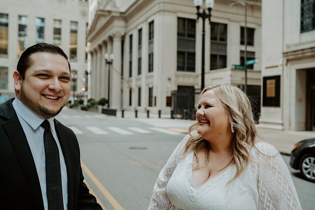 Bride looks at the Groom as he laughs towards the camera and they stand in the center of a Chicago street. 