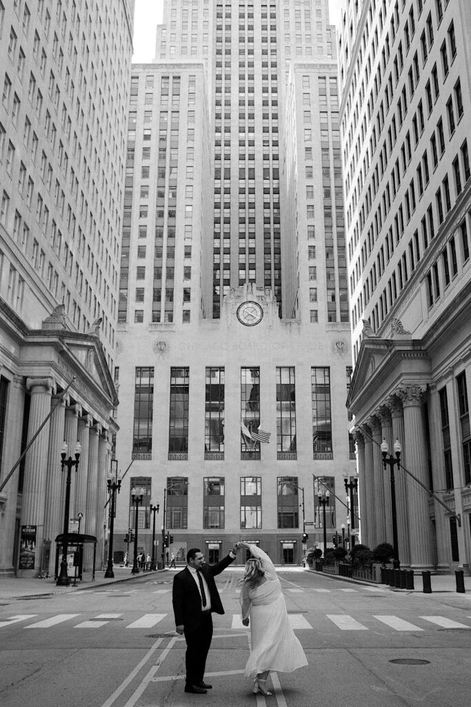 Groom spins Bride in the center of a street in front of Chicago Board of Trade Building and look at each other. 