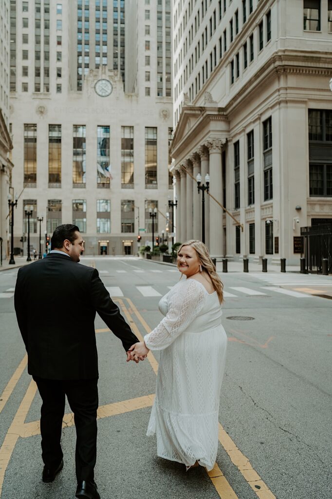 Bride and Groom walk in the center of a street towards the front of Chicago Board of Trade Building and look at each other. 