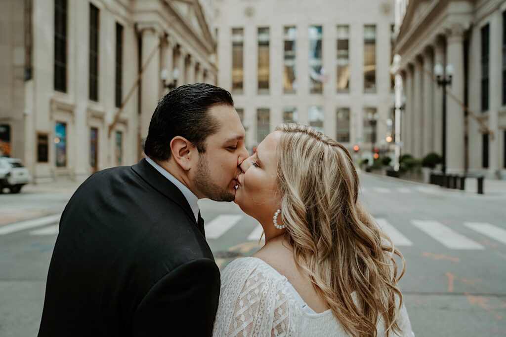 Bride and Groom kiss in the center of a street in front of Chicago Board of Trade Building and look at each other. 