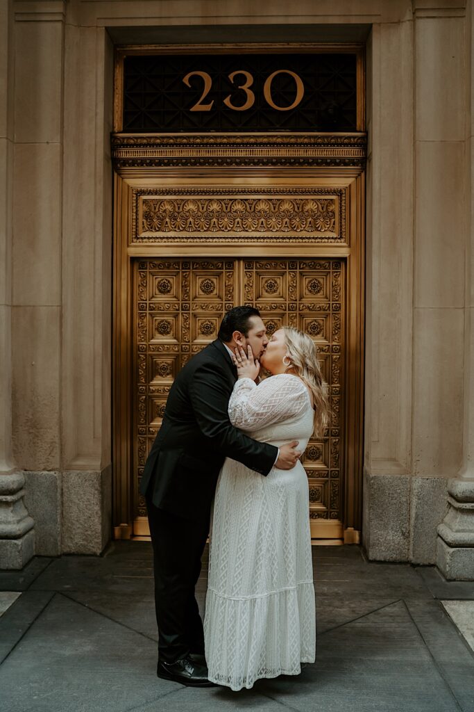 Bride and Groom embrace and kiss in front of an ornate gold door for elopement portraits in downtown Chicago. 