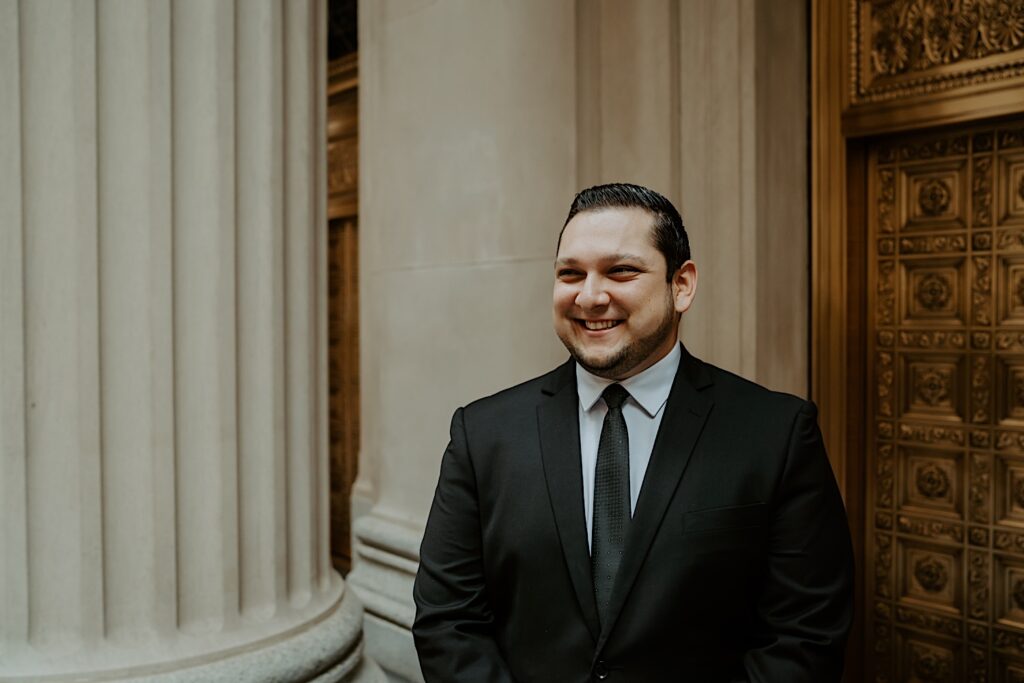 Groom smiles to the side as he stands in front of a gold ornate door for elopement portraits in downtown Chicago. 