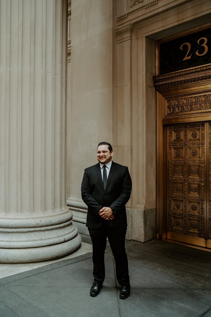 Groom stands in front of a gold ornate door for elopement portraits in downtown Chicago. 