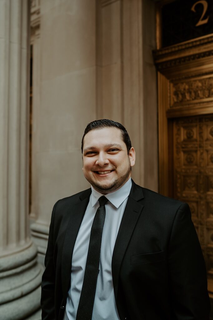 Groom smiles to the camera as he stands in front of a gold ornate door for elopement portraits in downtown Chicago. 