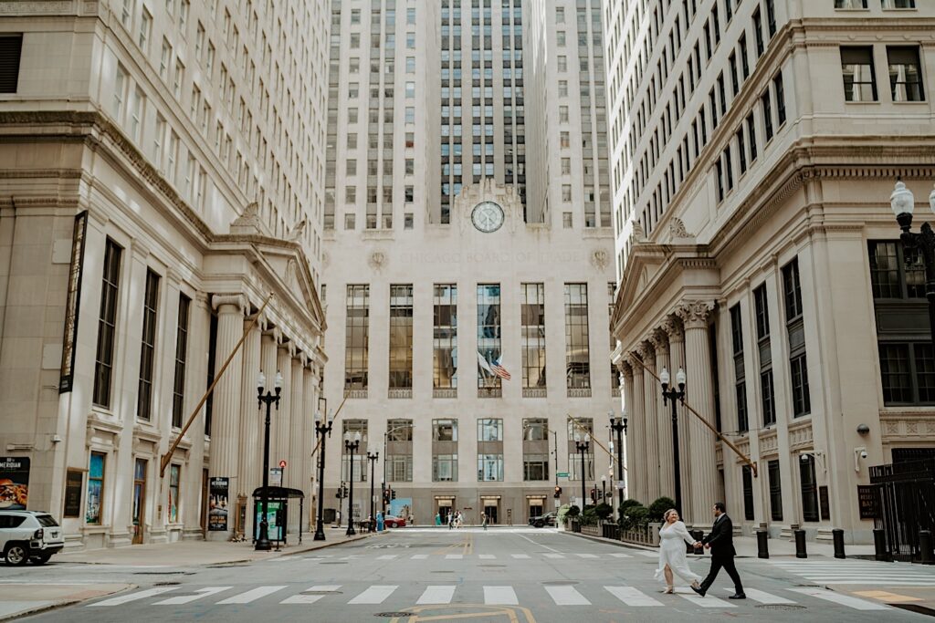 Bride and Groom cross the street in front of Chicago Board of Trade Building looking at each other. 