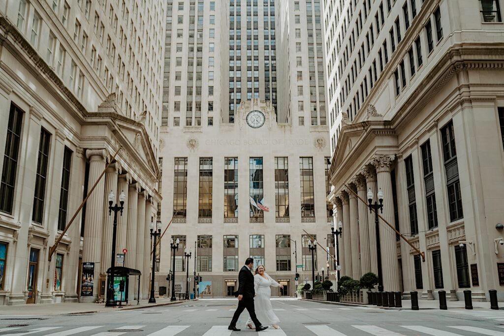 Bride and Groom cross the street in front of Chicago Board of Trade Building looking at each other. 