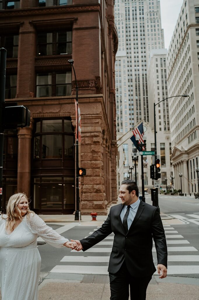 Bride and Groom hold their arms out and hold hands while walking down Chicago street.