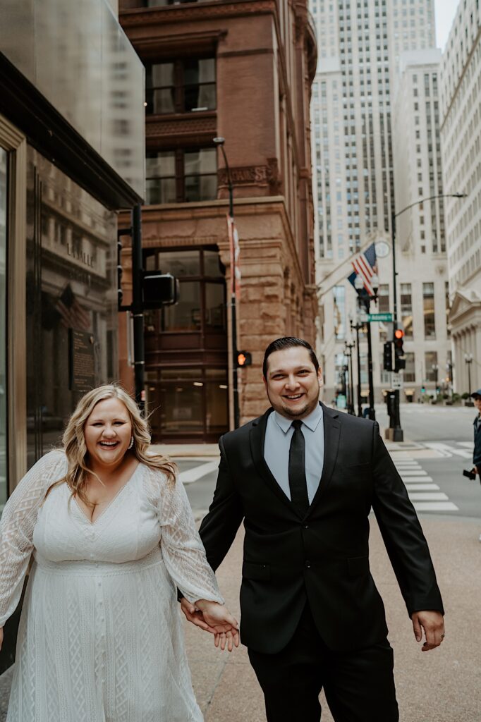 Bride and Groom smile towards the camera as they walk down the city sidewalk street during elopement portraits in Chicago. 