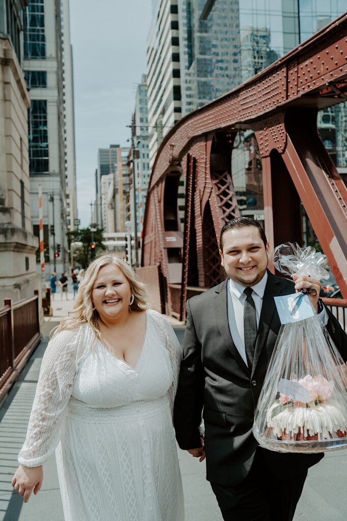 Bride and Groom cross Chicago bridge holding a bundt cake smiling. 