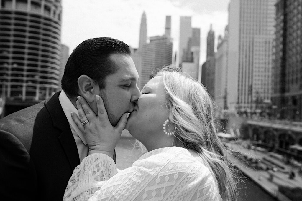 Bride and Groom embrace and kiss as they stand on a bridge overlooking the Chicago River with Chicago skyline in the background. 