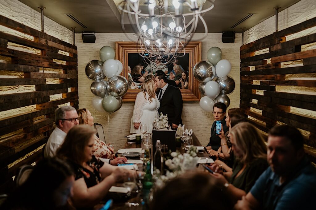 Bride and Groom kiss in-front of a table set up with their guests during their intimate restaurant reception in Chicago. 