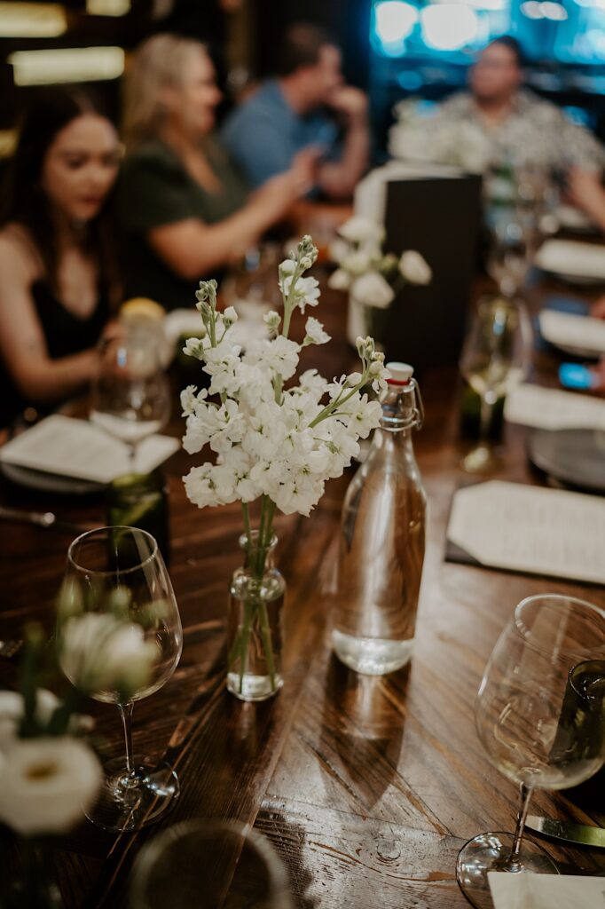 A vase of white flowers sit centered in a table with wine glasses around it. 