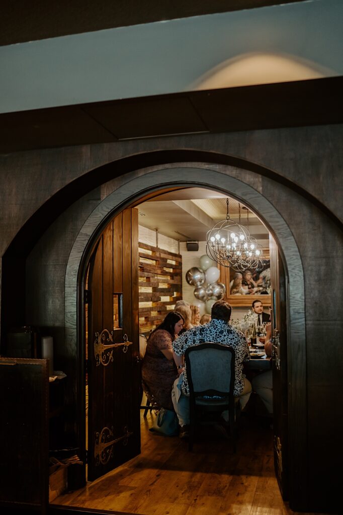 Midwest Elopement photographer captures a door leading to a private dining room where bride and groom's guests sit around a wooden table and enjoy the intimate reception in Chicago. 