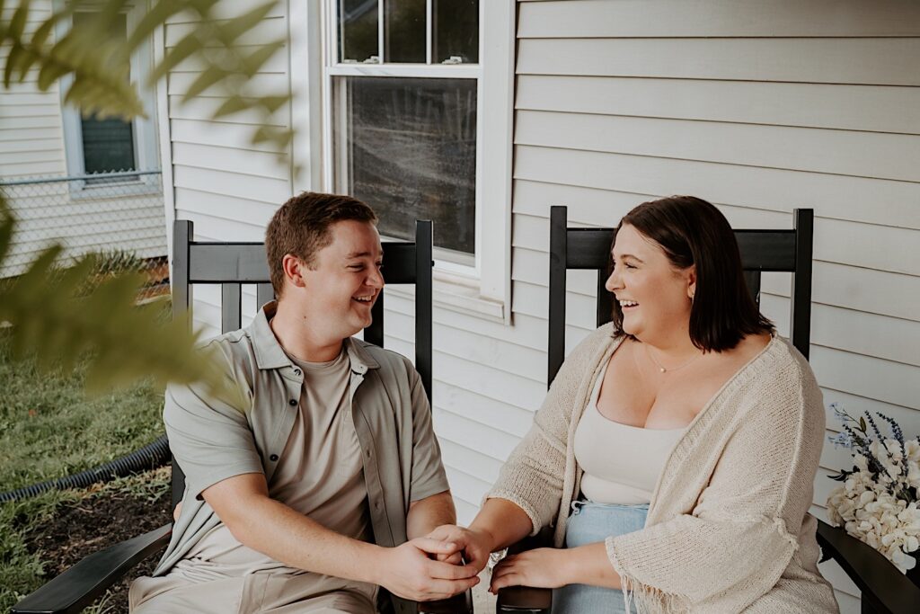 Couple sits on rocking chairs and holds hands while they look at each other during intimate couple portraits in Indiana.