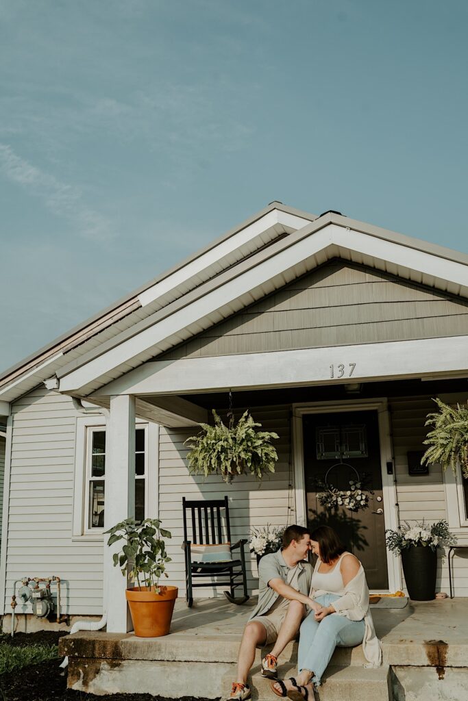 Couple sits on the front steps leading up to their porch to their house during intimate portraits on their house in Indiana during cozy portraits. 