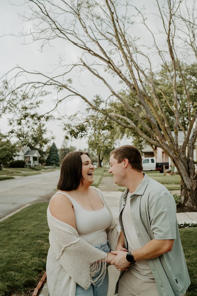 Couple walks down their sidewalk holding hands while candidly giggling during intimate portraits in Indiana.