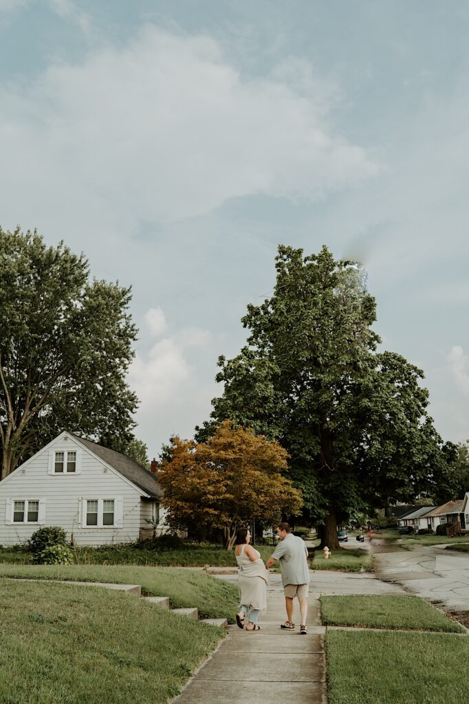 Couple walks down the sidewalks with their backs towards the camera for fun and cozy portraits in Indiana. 