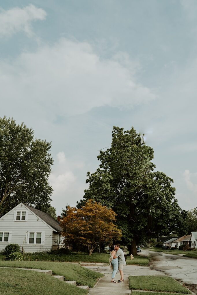 Couple walks down the sidewalk and kisses with their backs towards the camera for fun and cozy portraits in Indiana. 