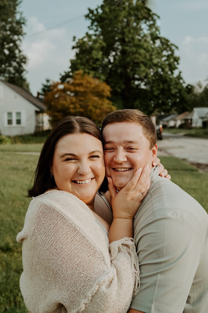 Woman holds her husbands face as they smile at the camera for candid portraits in Indiana. 