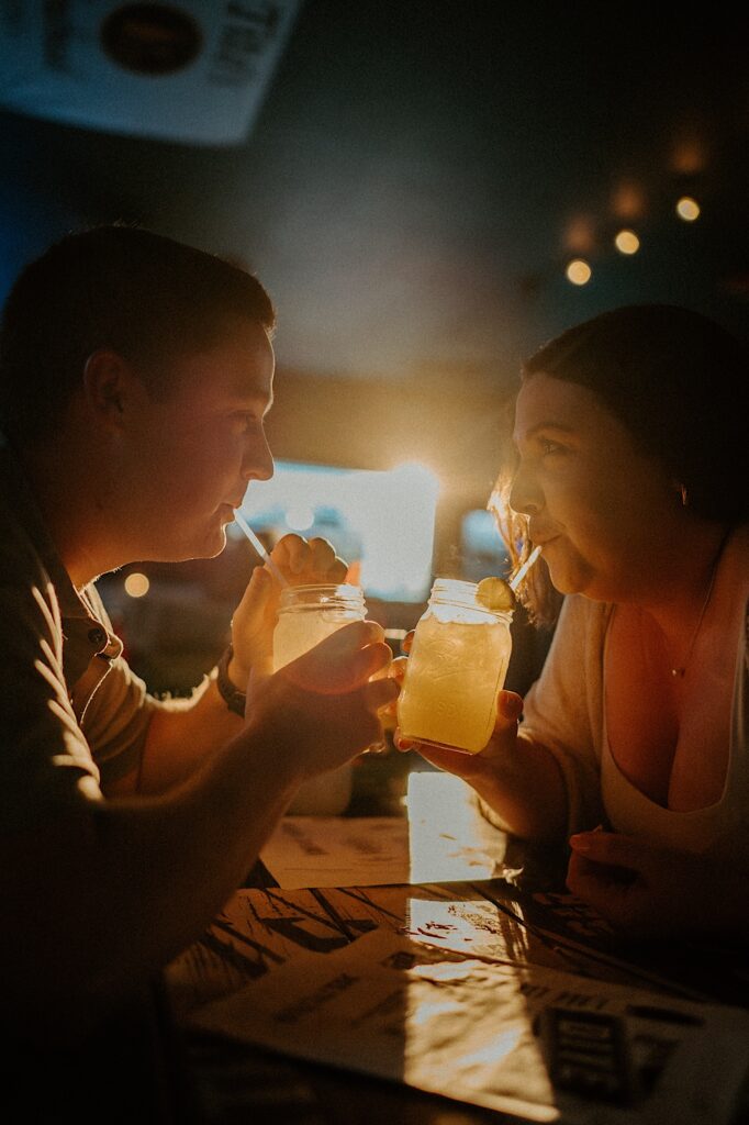 Couple looks at each other as they look at each other and sip out of straws in mason jars while sitting in Sixth St Dive Bar & Grill.