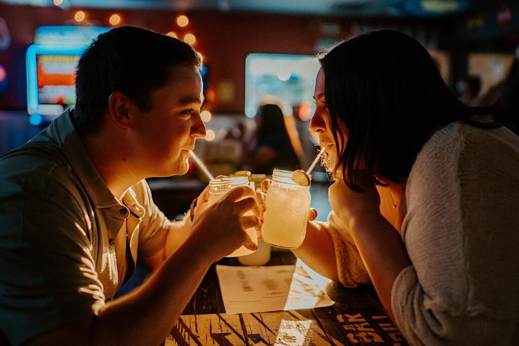 Couple looks at each other as they look at each other and sip out of straws in mason jars while sitting in Sixth St Dive Bar & Grill.