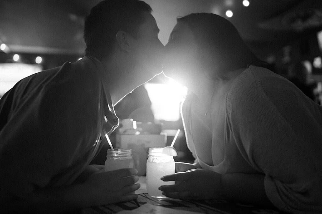 Couple kiss as they look at each other and sip out of straws in mason jars while sitting in Sixth St Dive Bar & Grill.