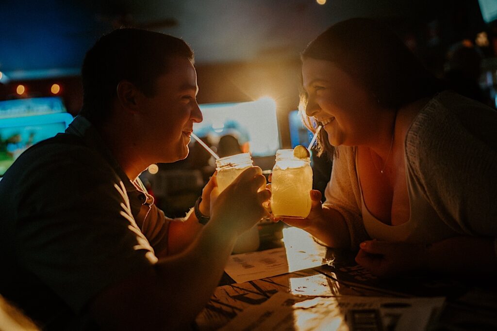 Couple looks at each other and smile as they look at each other and sip out of straws in mason jars while sitting in Sixth St Dive Bar & Grill.