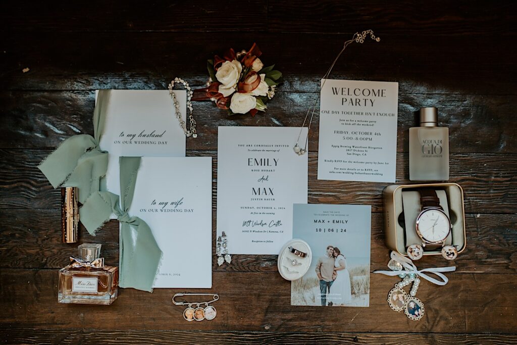 Wedding day details with gold accessories and sage green ribbon on a rustic wooden floor.