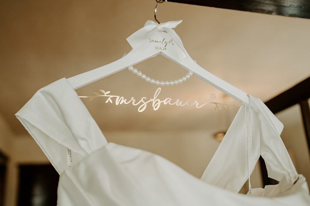 A bridal wedding hanger with white paint and pearl accents.  The hanger bar is made out of gold metal and has the outline of the brides married name on it.