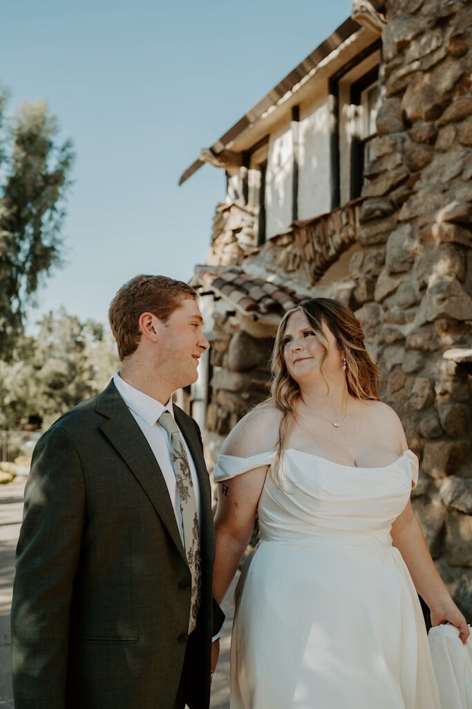 A bride and groom walk and hold hands outside of their California wedding venue Mt Woodson Castle. 