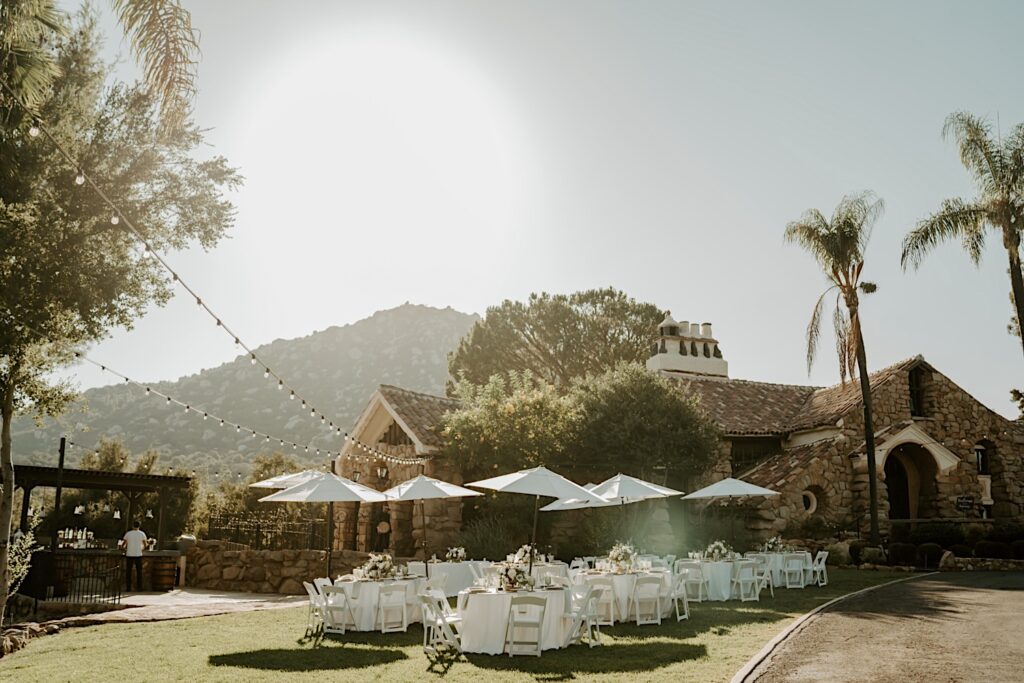 An outdoor wedding venue with white umbrellas over small tables and floral centerpieces in California.