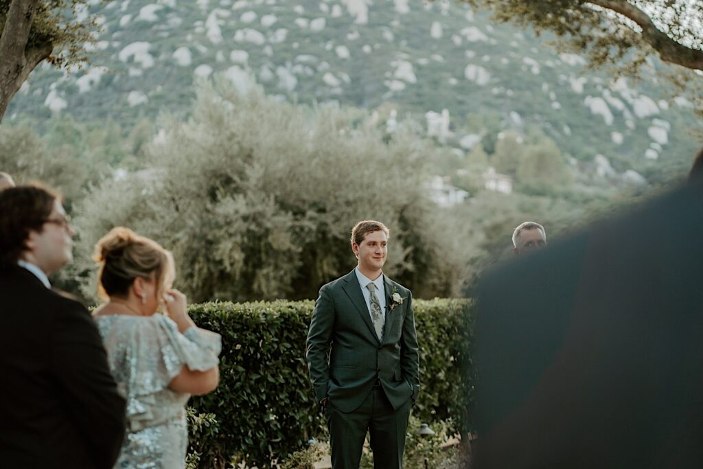 The groom waits for his bride before his wedding ceremony in the outdoor ceremony space at Mt Woodson Castle in California. 