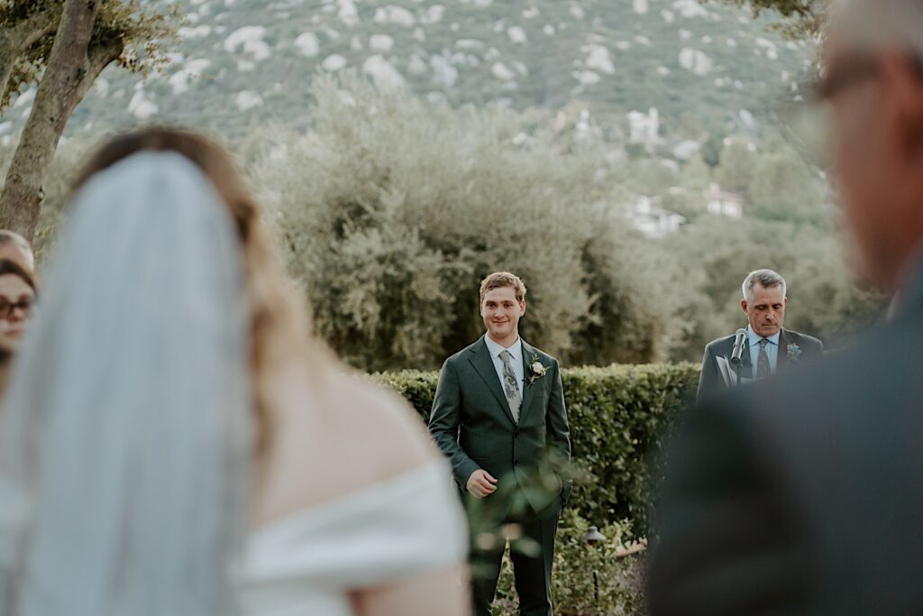 The groom waits for his bride before his wedding ceremony in the outdoor ceremony space at Mt Woodson Castle in California. 