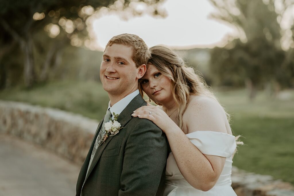 A bride holds onto her husbands shoulder as they both look towards the camera during their wedding portraits at their California wedding.