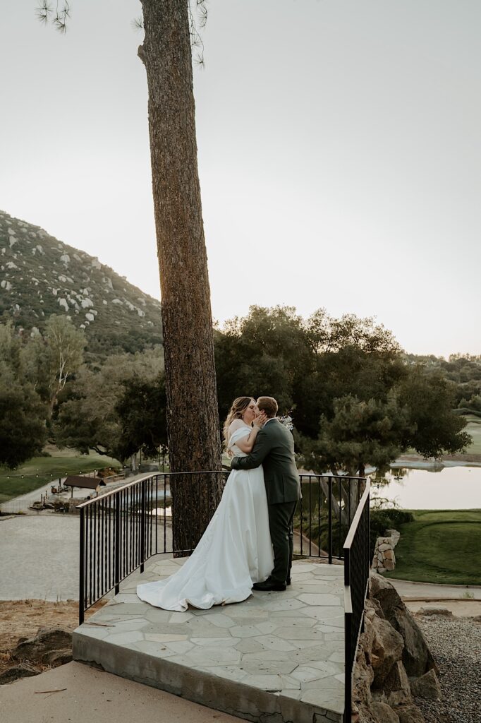 A bride and groom kiss and hold one another overlooking the golf course at Mt Woodson Castle in California. 