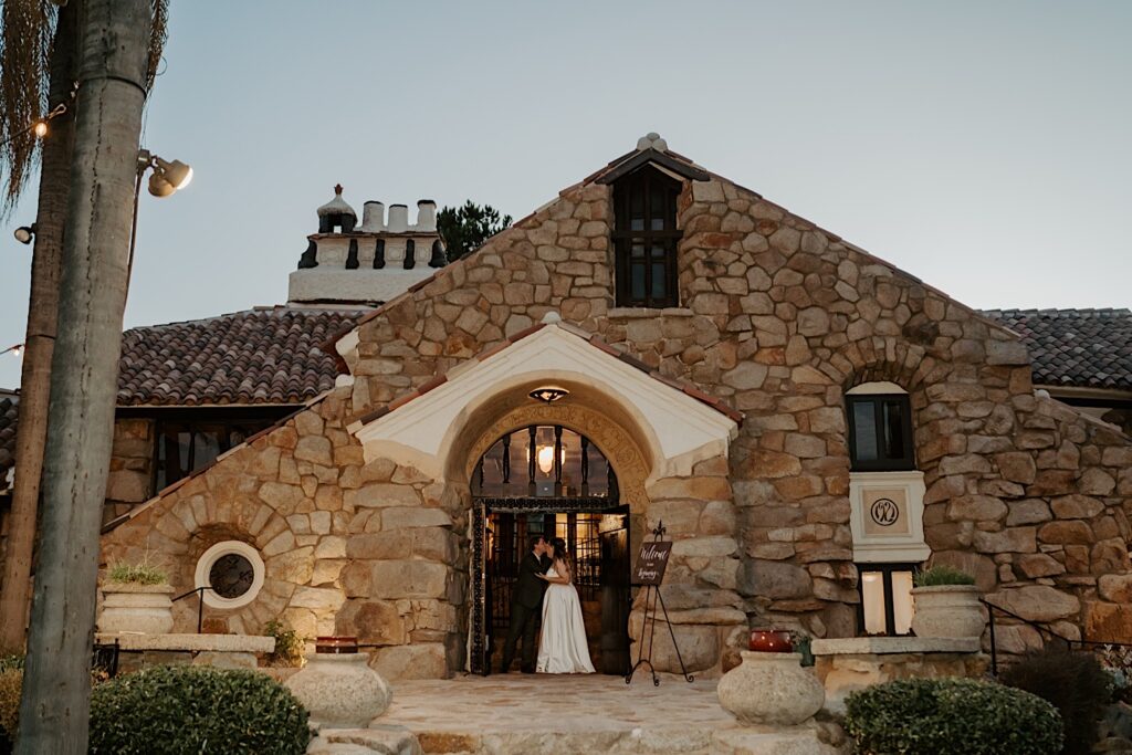 A bride and groom kiss standing in the entrance of their historic California wedding venue.