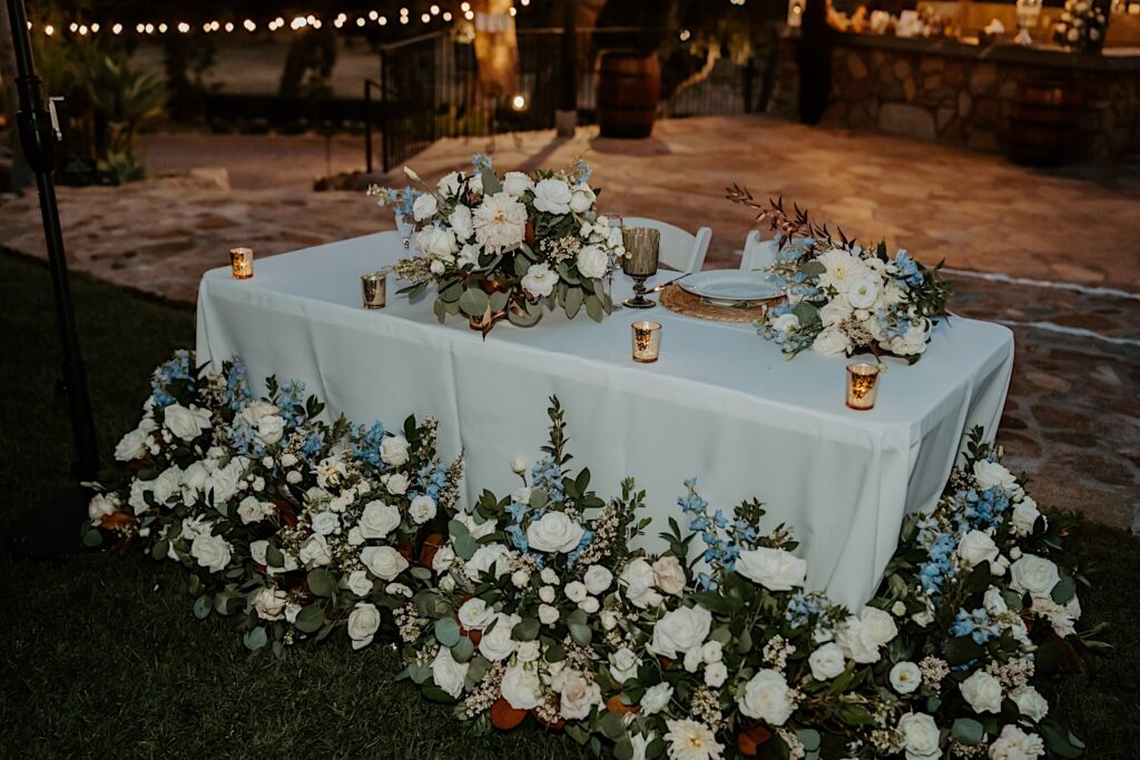 A white and blue floral installation in front of the bride and grooms sweetheart table made by Finest City Florals in California. 