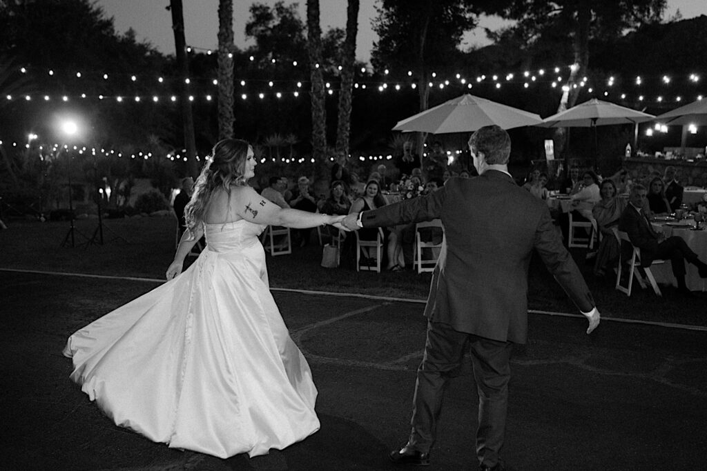 A bride and groom share their first dance as they walk into their wedding reception an outdoor space covered in string lights at Mt Woodson Castle in California.  